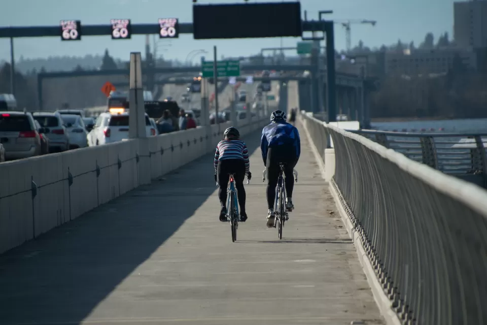 Two cyclists riding on a protected bike lane on a bridge in Seattle with traffic on their left.